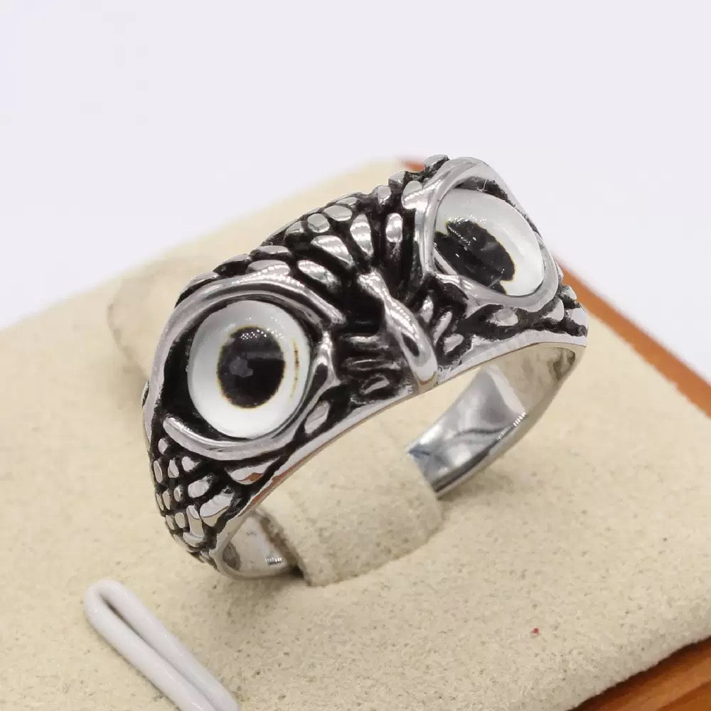 Silver owl-shaped ring on a beige cushion with a white background