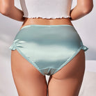 Person wearing light blue satin underwear with a white top on a neutral background