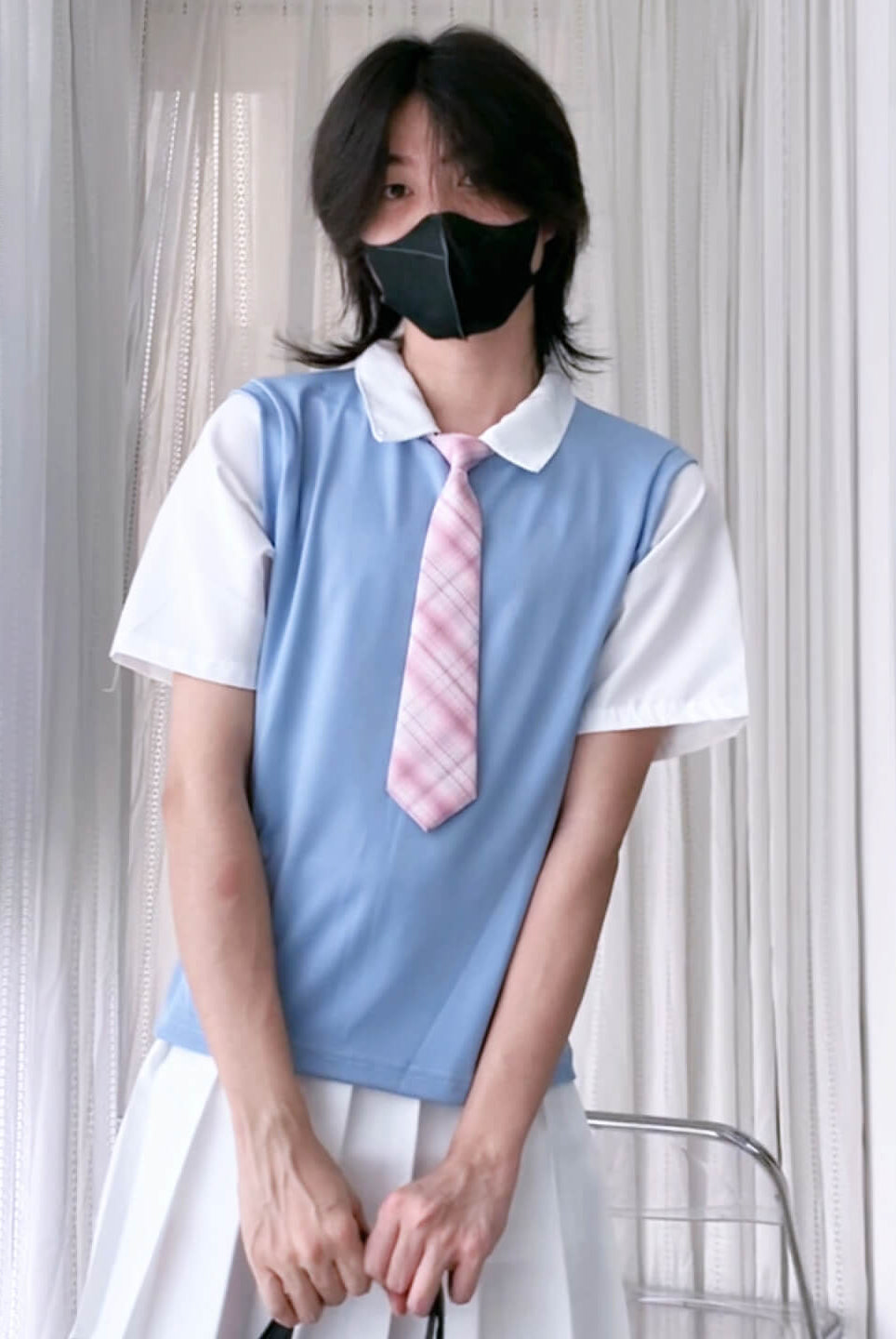 Person wearing a light blue vest over a white shirt with a pink tie, standing against a neutral background.