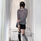 Person wearing a black and white striped sweater and skirt with matching knee-high socks in a minimal indoor setting.
