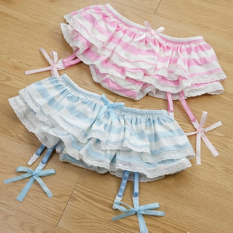 Two pairs of ruffled shorts, one pink and white striped, the other blue and white striped, on a wooden floor.