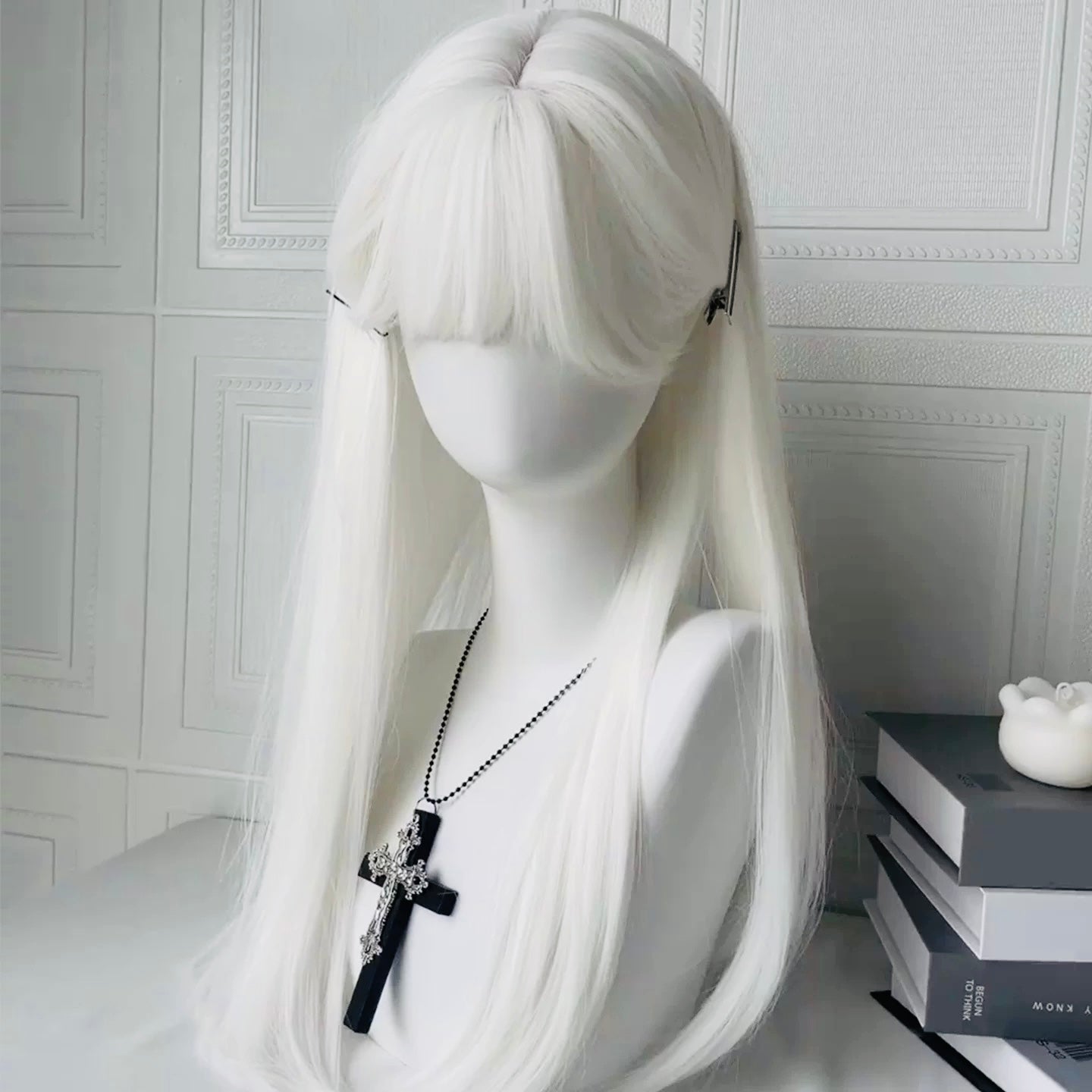 White femboy wig on a mannequin head with a cross necklace against a white wall.