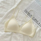 A cream-colored ribbed triangle bralette with thin straps, laid flat on a white textured fabric next to a printed magazine page.