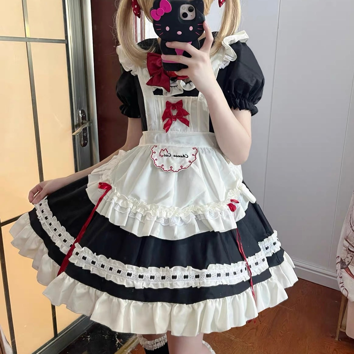 Person wearing a black and white maid outfit with red accents, taking a mirror selfie.