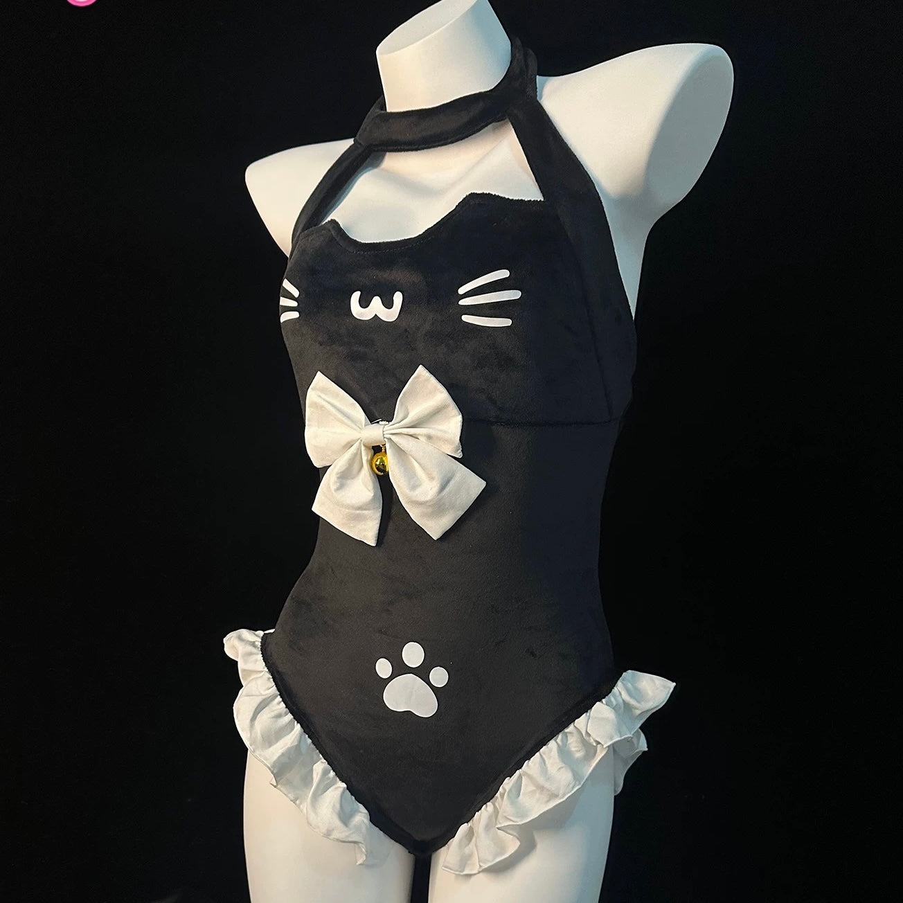 A black cat-themed halter bodysuit displayed on a white mannequin torso against a black background. The bodysuit features white cat face details, a large white bow with a small gold center, white paw print, and white ruffled trim at the waist.