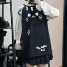 A femboy wearing a black cat-face print mini dress over a white long-sleeve shirt, standing in front of a mirror in what appears to be a boutique.