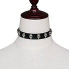 A black faux-leather choker collar decorated with silver skull studs, displayed on a white fabric mannequin bust.