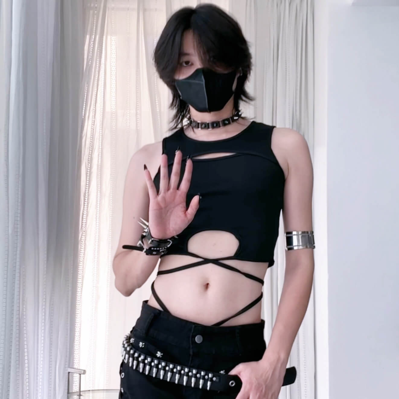 Person wearing a black sleeveless top with cut-out design and black gloves, standing against a plain background.