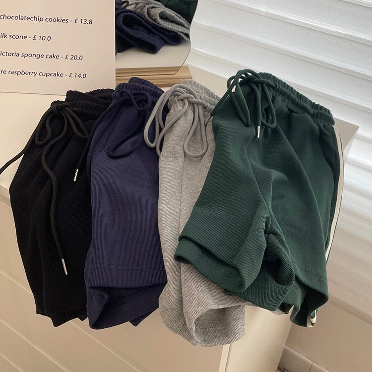 Four pairs of shorts in black, navy, gray, and green on a mannequin against a blurred background.