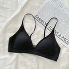A black ribbed knit triangle bralette with thin adjustable straps, laid flat on a white textured fabric surface next to a printed magazine page.