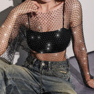 Person wearing a sheer fishnet top and beige pants against a plain background
