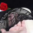 Black lace fabric held by a hand with a red rose in the background