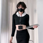 Femboy wearing a black outfit with a white shirt, holding a tablet, against a light curtain background.