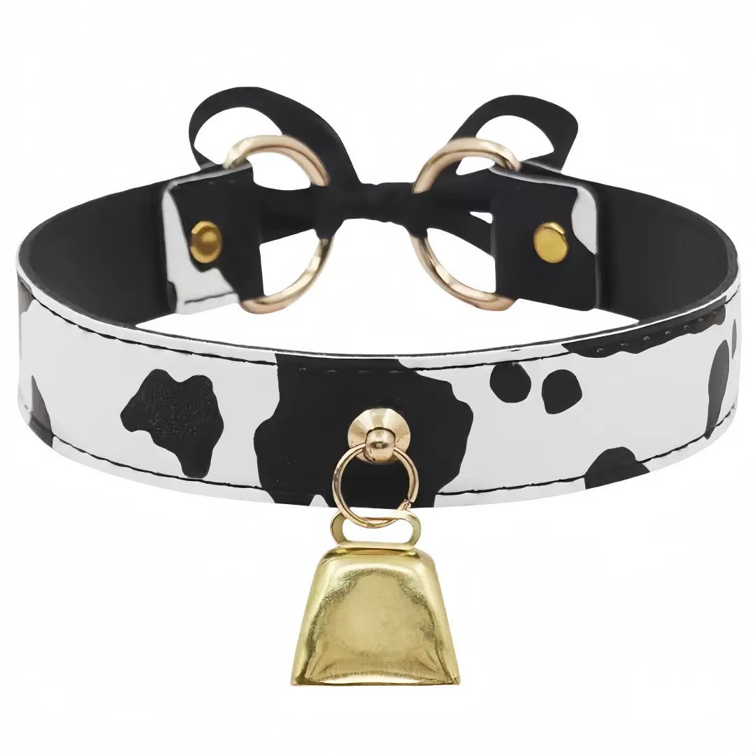 A cow-print faux leather collar with black and white spots, featuring a black bow at the back, gold-tone metal rings, and a hanging gold bell.