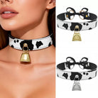 A split image showing a cow-print choker collar worn by a model on the left, and two product views on the right: one with a gold bell and bow, and one with a silver bell and bow. The collar has a black and white cow print pattern with a black faux-leather strap, white stitching, a black bow, and a bell charm.