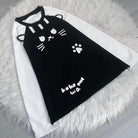 A black and white raglan long-sleeve shirt featuring a cute cat face, whiskers, paw print, and 'kuku wa' text on the front, laid flat on a white faux fur rug.