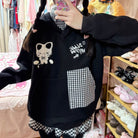 Person wearing a black hoodie with white text and graphics, standing in a room with shelves of shoes and clothes.