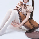 Femboy wearing a brown maid outfit with white stockings sitting on a white surface.