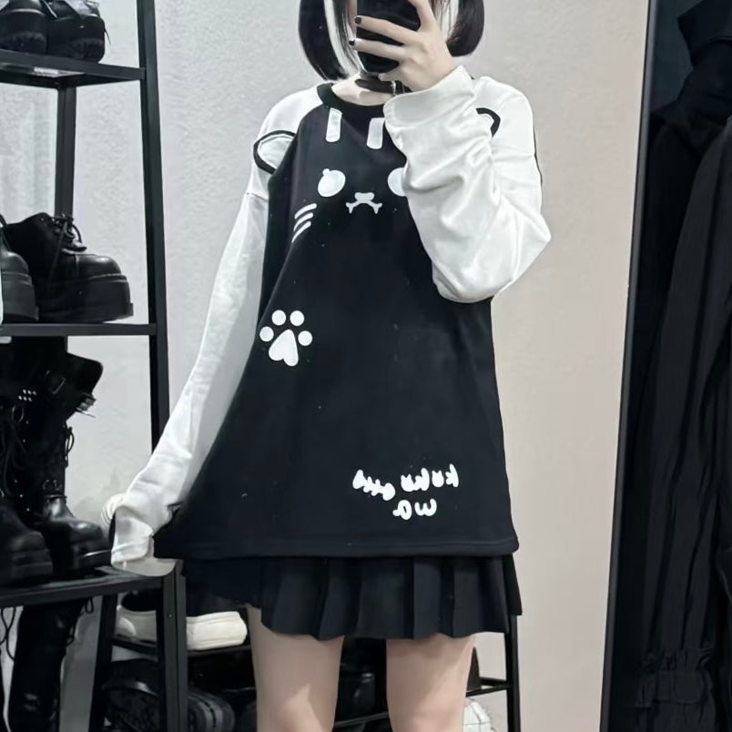 A femboy taking a mirror selfie in a clothing store wearing a black and white outfit. The outfit consists of a black pinafore-style dress with white graphic prints (cat face, paw print, and text) layered over a white long-sleeve shirt, and a black pleated mini skirt.
