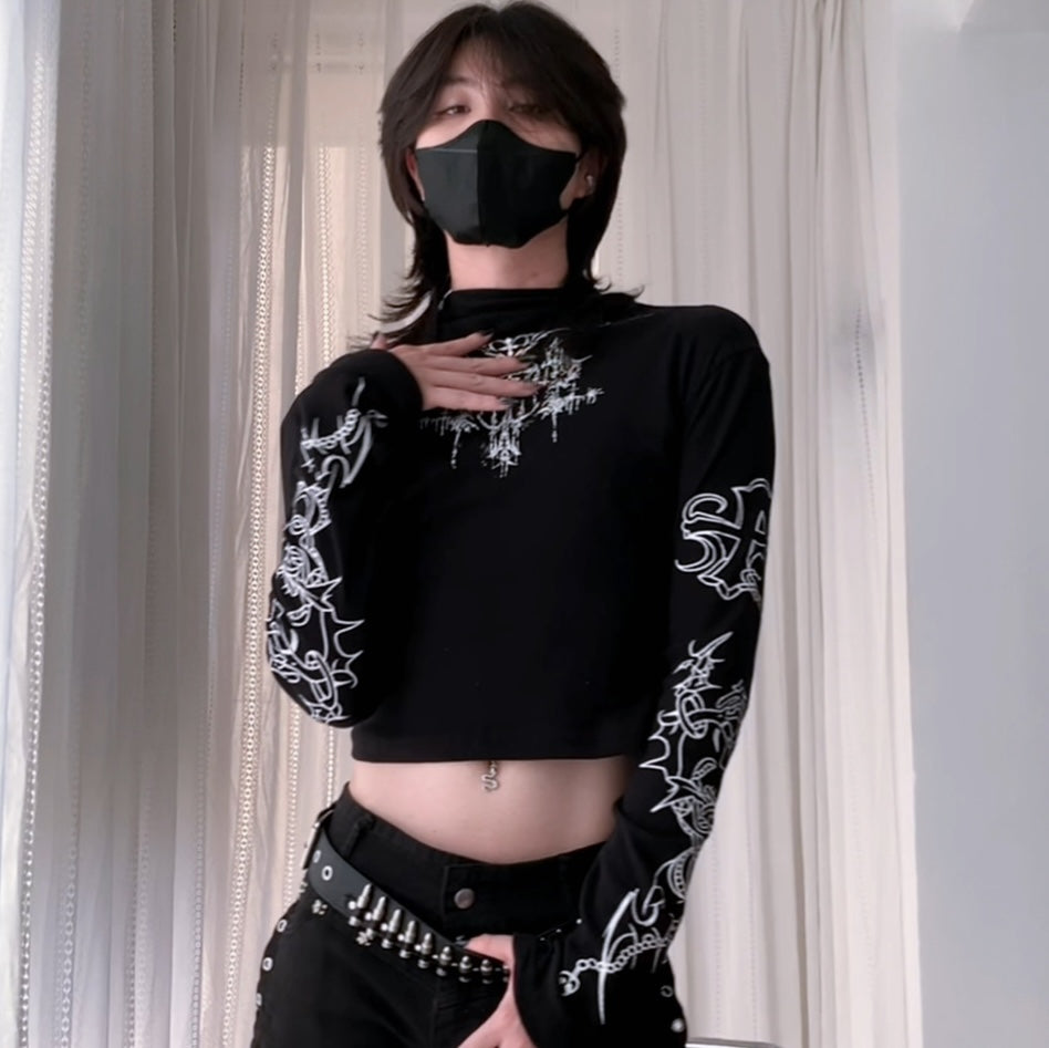 Person wearing a black crop top with a sun and moon design, black skirt, and striped sleeves against a white curtain background.