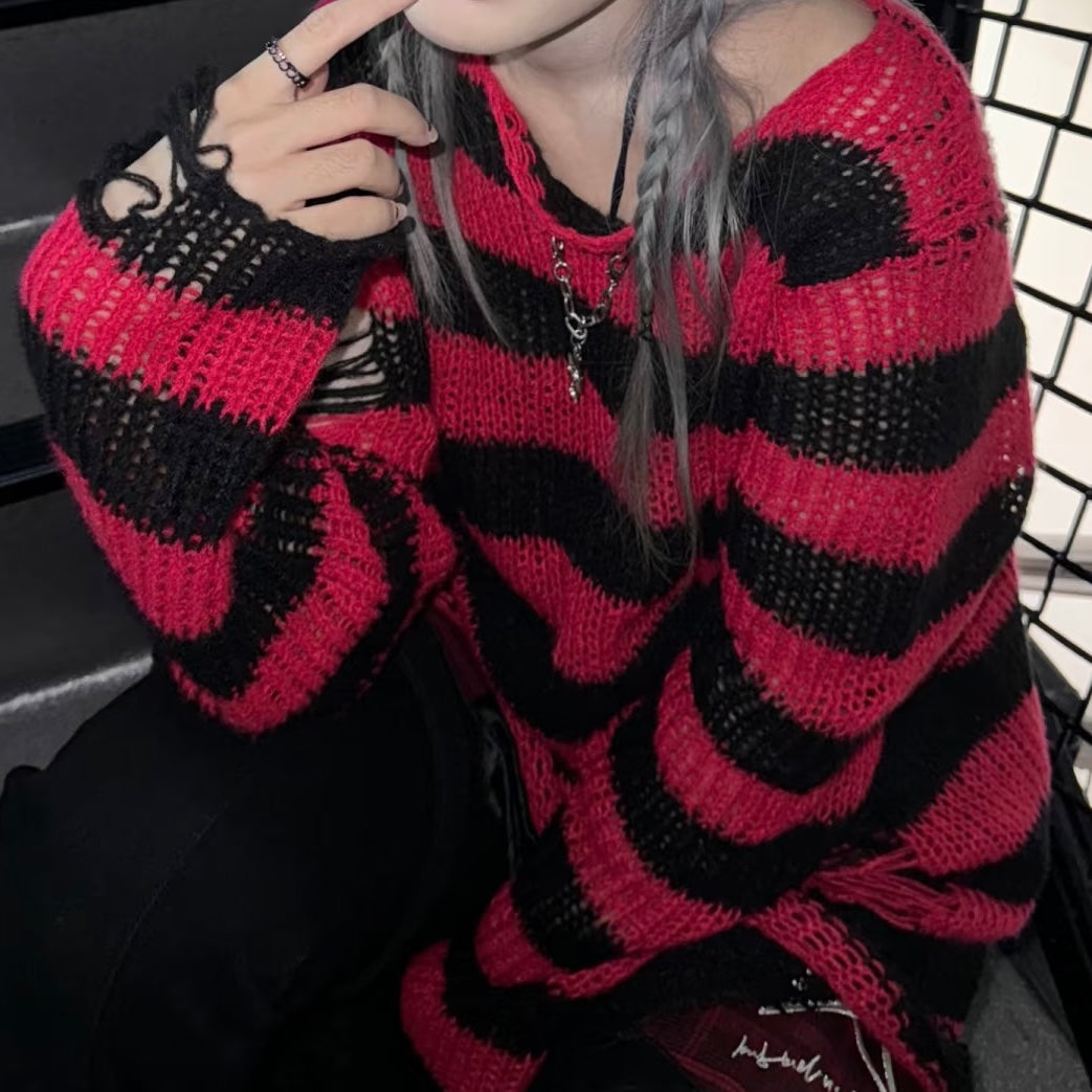 A person wearing a chunky knit sweater with bold horizontal red and black stripes, seated in a dark interior with a black grid chair visible in the background.
