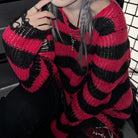 A person wearing a chunky knit sweater with bold horizontal red and black stripes, seated in a dark interior with a black grid chair visible in the background.