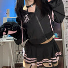 A femboy wearing a black  crop hoodie and mico skirt set, holding a black plush toy in a room setting.
