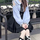 Person wearing a black skirt and blue blouse with ruffled details sitting on a bench.