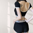 Person wearing a black sports bra and shorts with visible tattoos on a white background