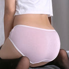 Femboy wearing a white top and light purple underwear with a neutral background