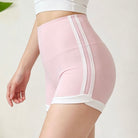 A close-up of a model wearing high-waisted light pink athletic shorts with white side stripes and a white inner leg band, paired with a white sports bra against a light neutral background.