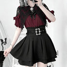 A model wearing a gothic-style dress with a deep burgundy blouse, black lace flutter sleeves, a black waist belt with silver rhinestone embellishments, and a black pleated skirt.