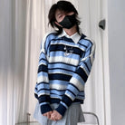A femboy wearing a blue, navy, and white striped knit sweater with a white collared shirt underneath, a black face mask, and a gray pleated skirt, standing in front of white curtains.