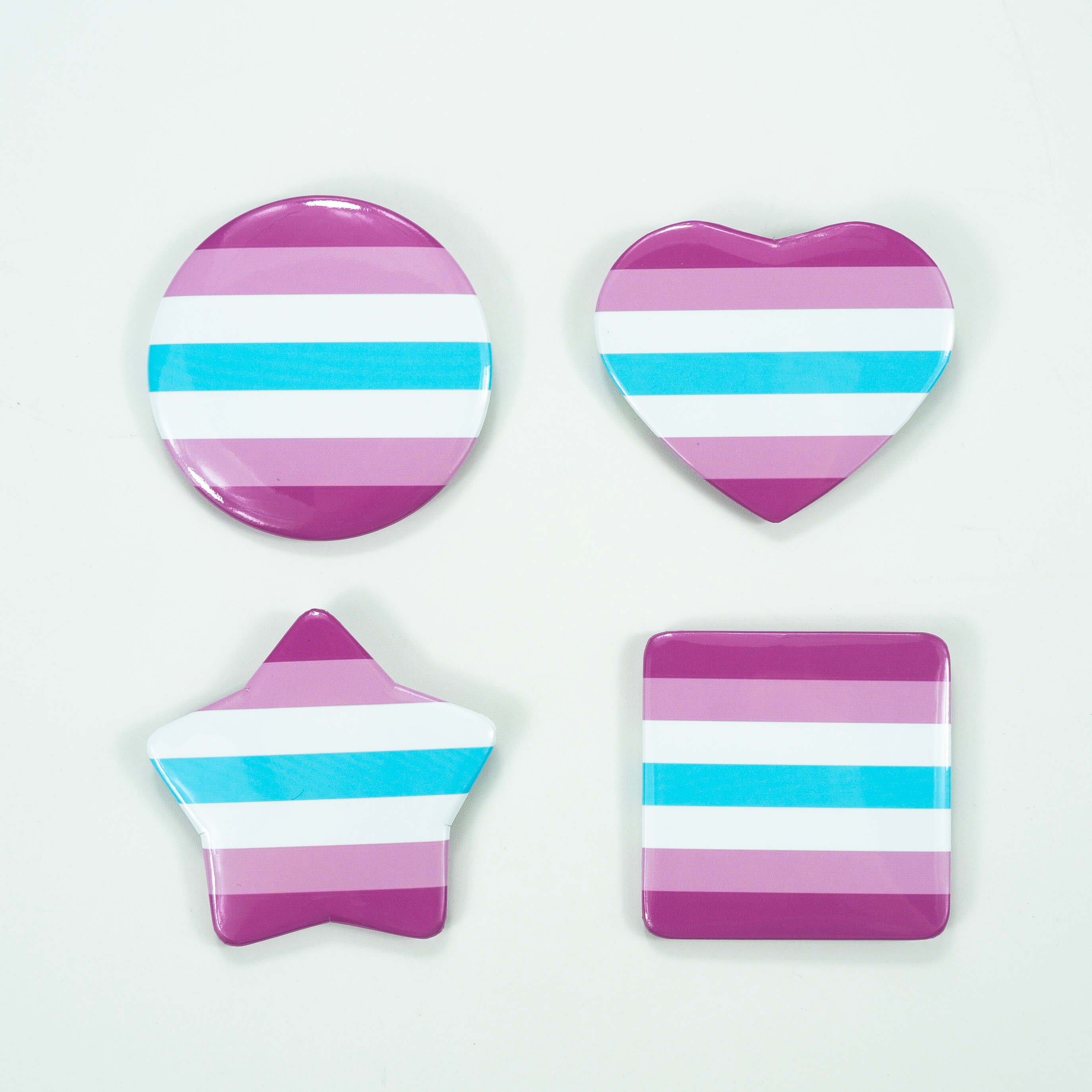 Femboy pride flag pins in heart, star, and square shapes on a white background