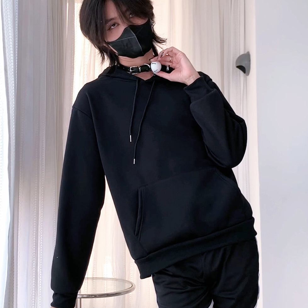 Femboy wearing a black hoodie and pants with a mask indoors.