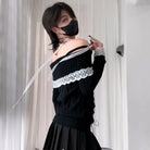 A femboy wearing a black off-the-shoulder ribbed sweater with a wide white lace band across the chest and matching lace cuffs, paired with a black pleated skirt, standing indoors in front of white curtains.