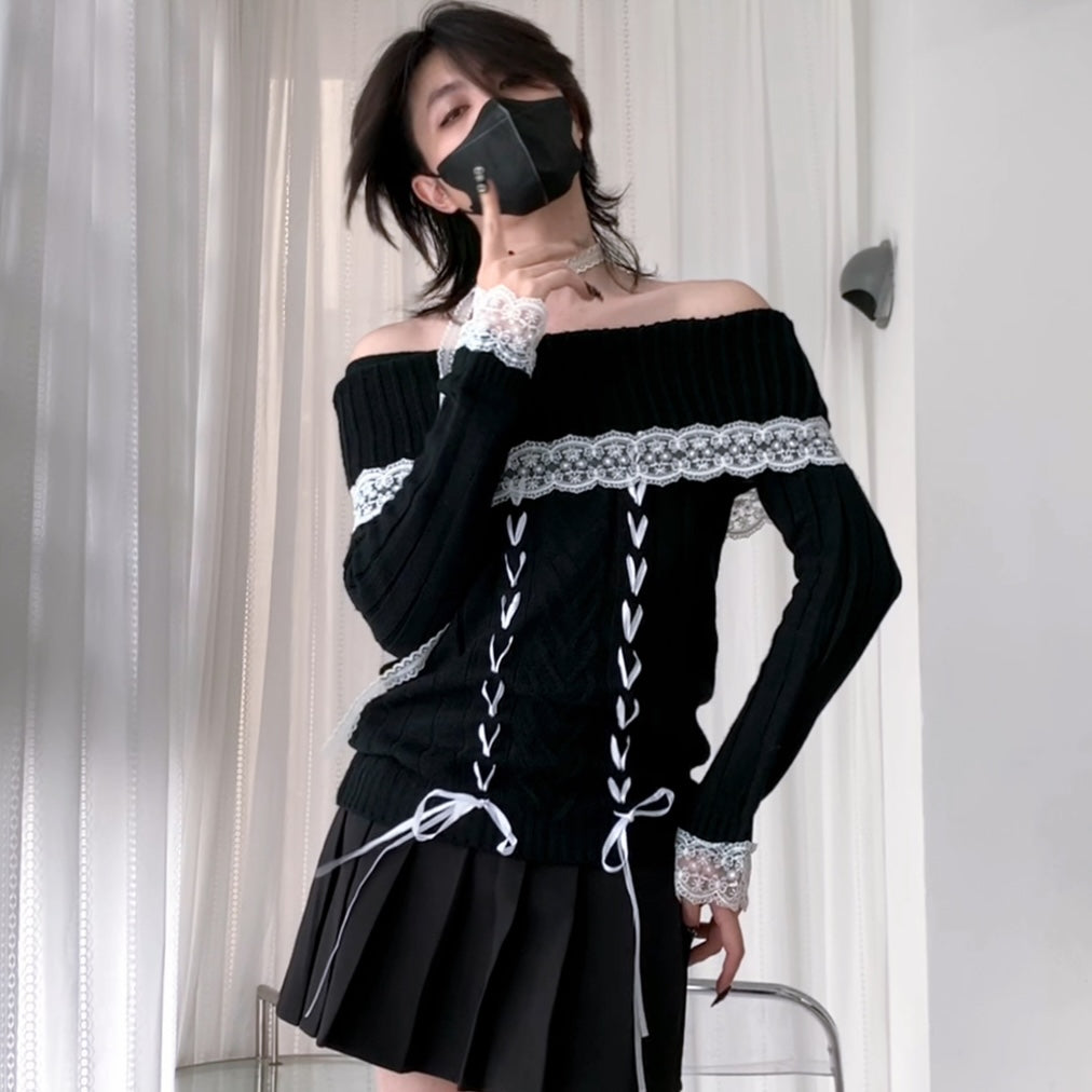 A femboy wearing a black off-the-shoulder knit sweater with white lace trim and front lace-up detailing, paired with a black pleated skirt, standing indoors near white curtains.