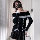 A femboy wearing a black off-the-shoulder knit sweater with white lace trim and front lace-up detailing, paired with a black pleated skirt, standing indoors near white curtains.