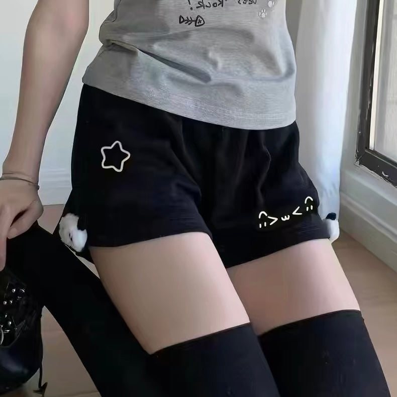 Femboy wearing black shorts with white designs and a gray top indoors.