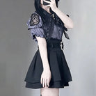 A femboy wearing a black and gray gothic Lolita-style outfit, featuring a short puff-sleeve top with lace shoulder details and a pleated black skirt, photographed against a neutral gray background.