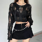 Person wearing a black outfit with sheer sleeves and a skirt, standing against a plain background.