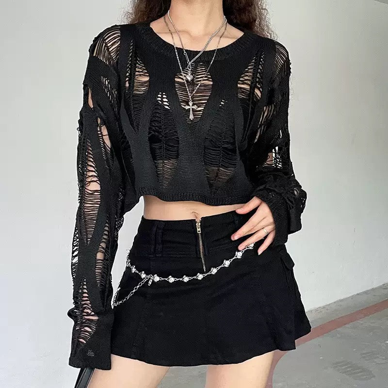Person wearing a black outfit with sheer sleeves and a skirt, standing against a plain background.