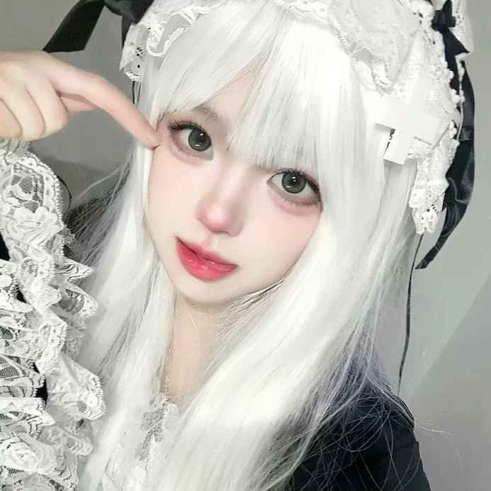 Person with white hair and decorative headpiece pointing to their eye, wearing a black and white outfit.