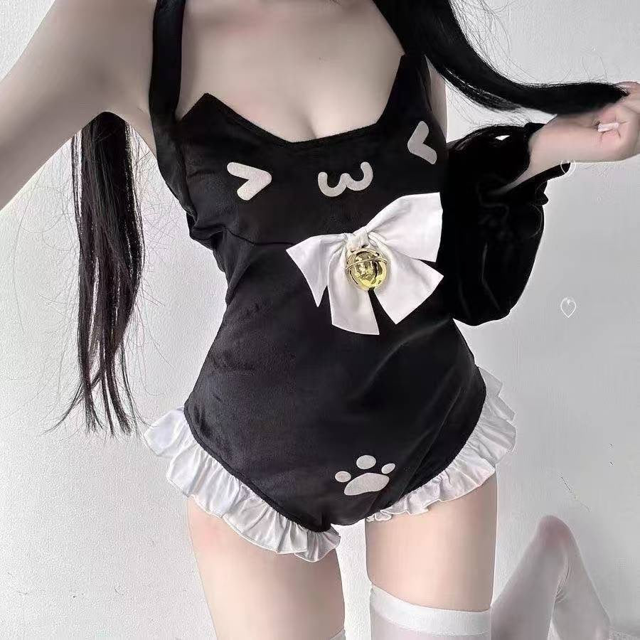 A femboy wearing a black cat-themed one-piece swimsuit or costume with white ruffled trim, a large white bow with a gold bell, and white cat face and paw print graphics, photographed against a plain light background.