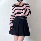 Person wearing a pink and black striped sweater with a black skirt on a plain background