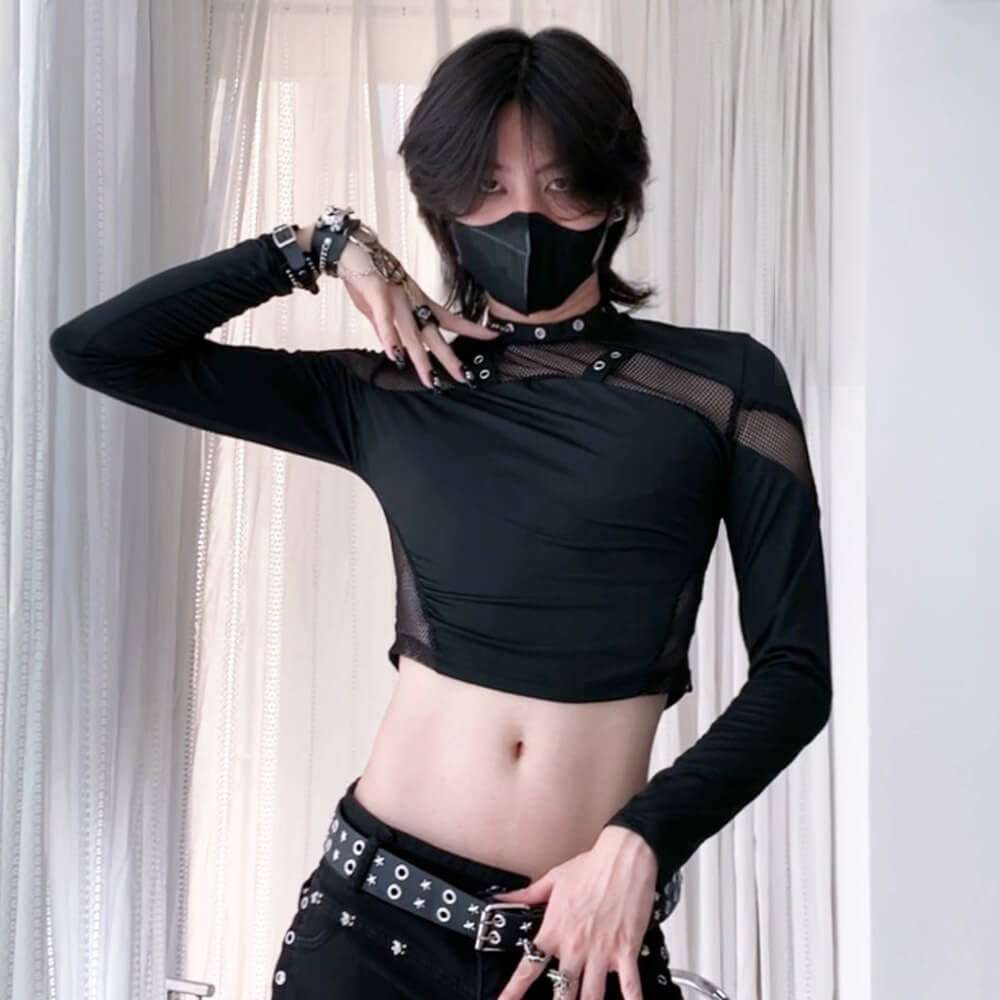 Person wearing a black long-sleeve top with mesh panels and black pants against a white curtain background.