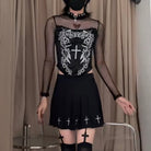 Person wearing a black outfit with white designs in front of beige curtains