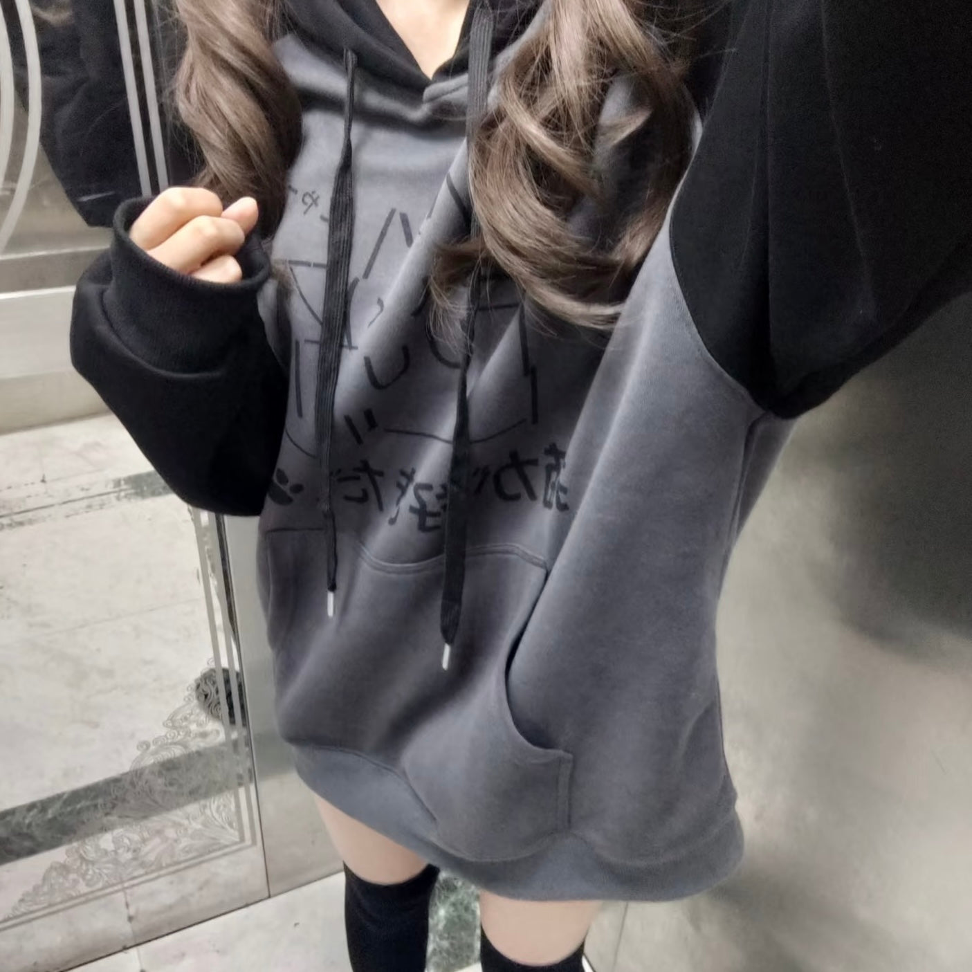 Person wearing a gray hoodie with black text design, standing on a tiled floor.