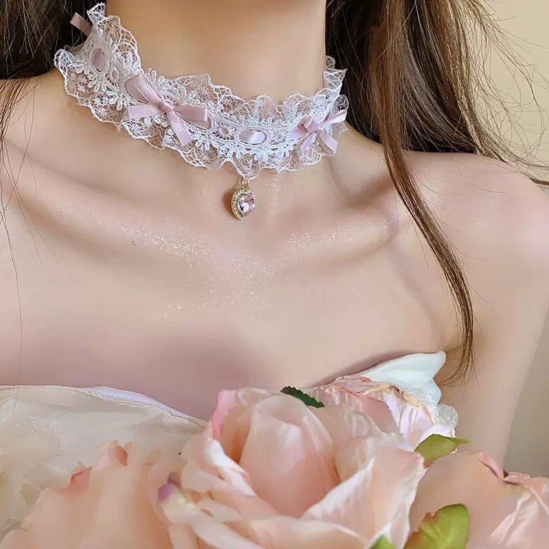 Close-up of a lace choker necklace with a pendant, held by a person wearing a light-colored dress with floral details.
