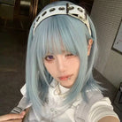 Person with light blue hair wearing a white outfit in an indoor setting